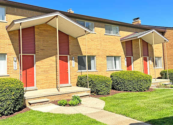 A row of red and white apartment buildings with green bushes in front.