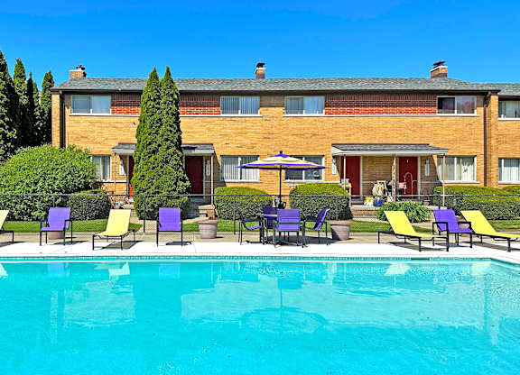 A swimming pool in front of a building with chairs around it.