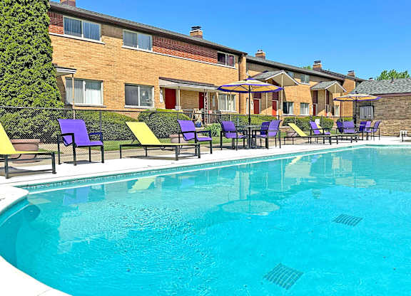 A swimming pool surrounded by purple chairs and yellow cushions.
