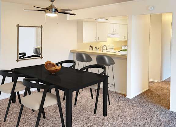 A black dining table with four chairs and a fan in a white room.
