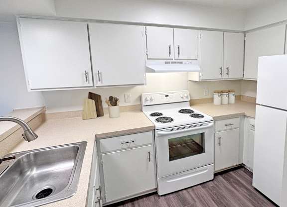 A white kitchen with a stove, sink, and refrigerator.