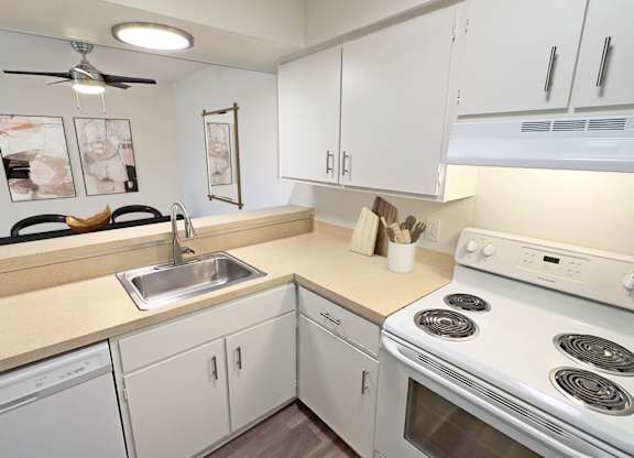 A white kitchen with a stove, sink, and cabinets.