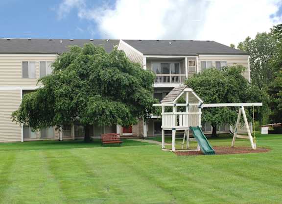 A playground with a slide and a swing set in front of a building.