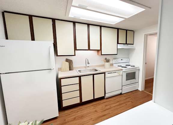 A kitchen with white appliances and wooden floors.