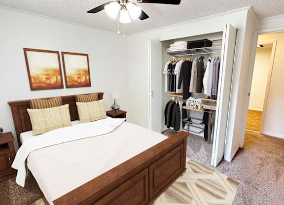 A bedroom with a large bed and a closet with clothes hanging.