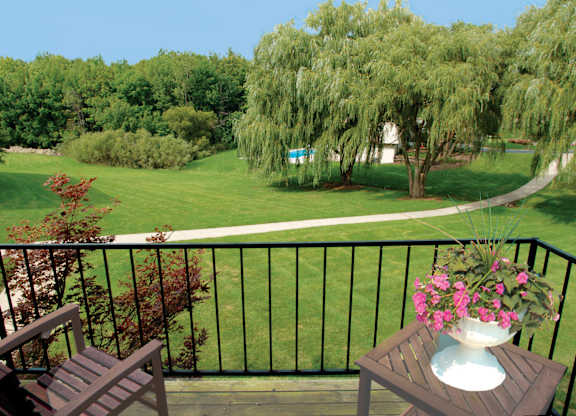 A balcony with a table and chairs overlooking a green lawn.