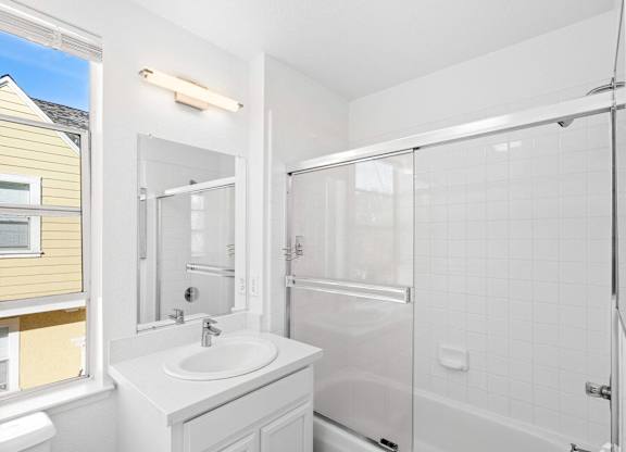 A white bathroom with a sink, mirror, and shower at Westmont Place Townhomes Apartments, Santa Cruz, California