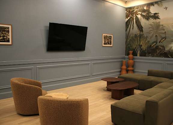 A room with a large painting of a jungle scene on the wall and a flat screen TV mounted above a sofa.