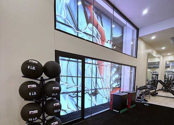 A gym with a row of weighted balls and a large screen showing a workout.