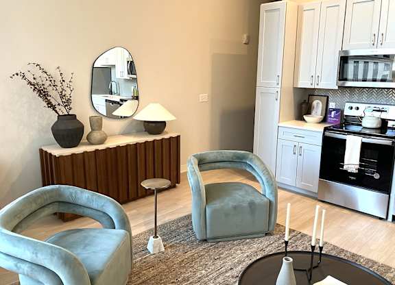 A modern living room with a grey armchair, a round mirror, a wooden cabinet, and a grey rug.