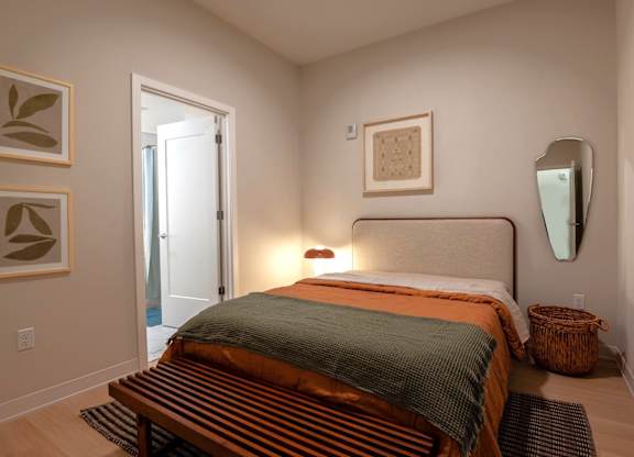 A bedroom with a bed, a mirror, and two wall art pieces.
