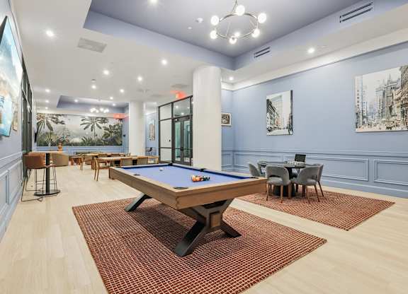 A pool table is in the middle of a room with a blue wall and a painting of a cityscape. at LiveWell Apartments, Pittsburgh