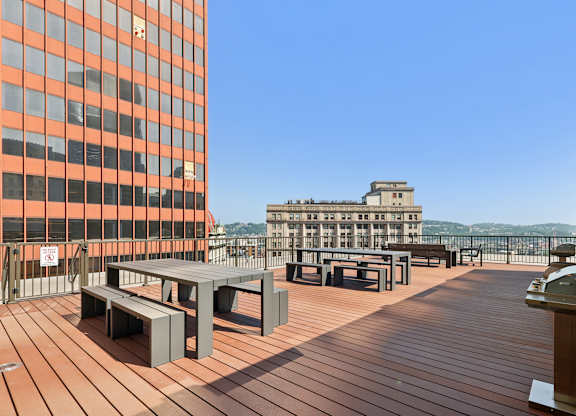 A wooden deck with benches and a table with a building in the background. at LiveWell Apartments, Pittsburgh, PA