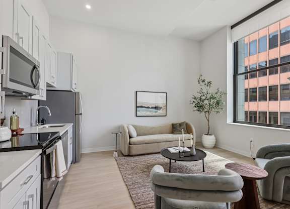 A modern kitchen with a large window and a living room area with a couch and chairs at LiveWell Apartments, Pennsylvania, 15222