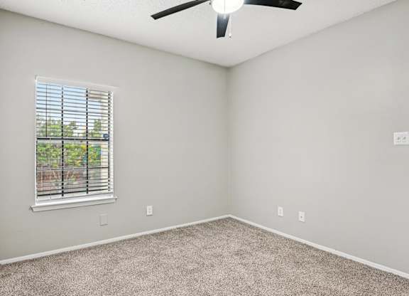 A room with a ceiling fan and a window with blinds.
