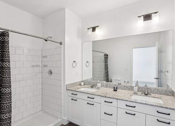 A bathroom with a white tile shower and a marble countertop.