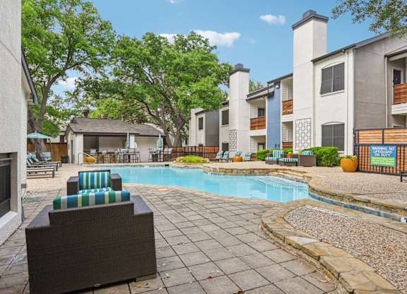 A pool surrounded by patio furniture and buildings.