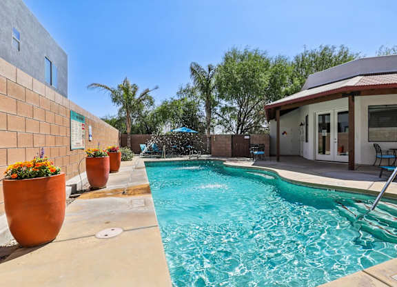 A pool with a waterfall and a patio area with chairs.