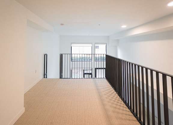 A room with a carpeted floor and a balcony with a railing.