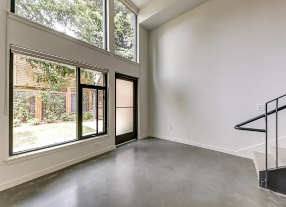 A room with a staircase and a view of the backyard through the windows.