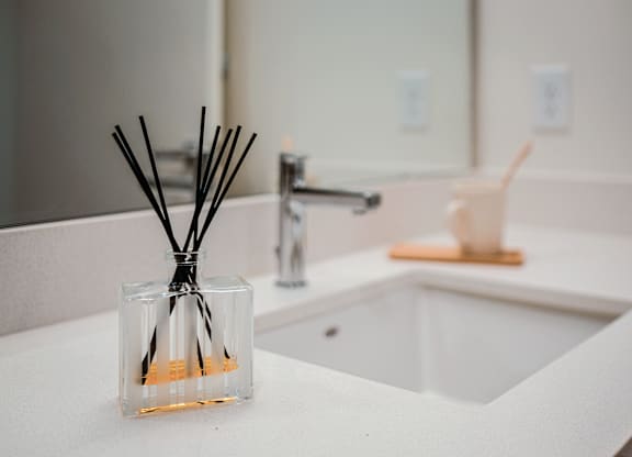 A glass container with reed sticks sits on a white countertop.