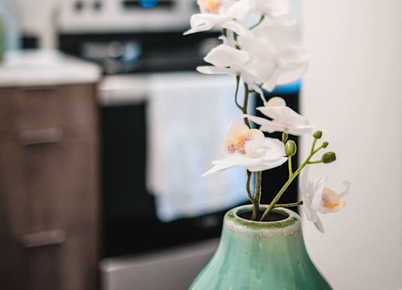 A green vase with white flowers sits in front of a microwave.