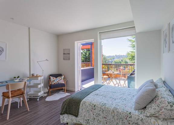 A bedroom with a bed, desk, chair, and a view of the backyard through the open door.
