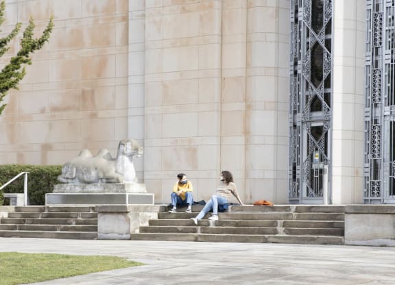 two people sitting on the steps of a building with a lion statue