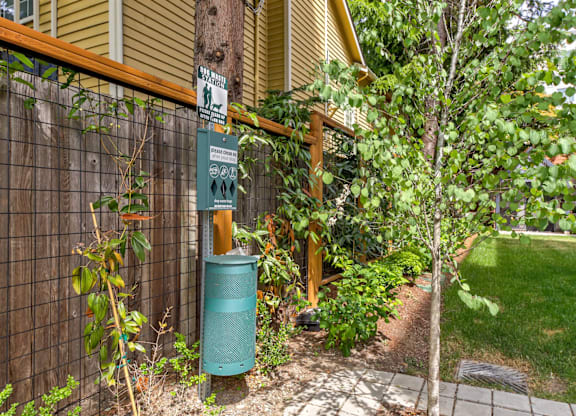 A green trash can sits next to a tree in a backyard.