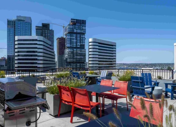 a rooftop patio with tables and chairs and a grill and a city in the background