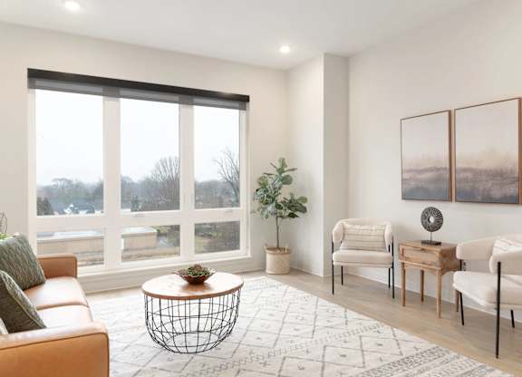 A living room with a large window, a sofa, a coffee table, and a potted plant.