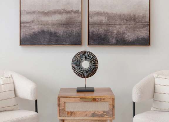 Two framed pictures hang on a wall above a fan and a table.