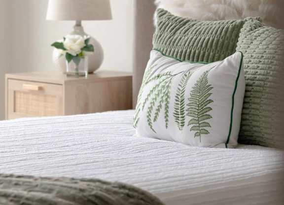 A bed with a white comforter and green pillows with leaf patterns.