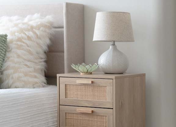 A white lamp with a green plant on a wooden nightstand.