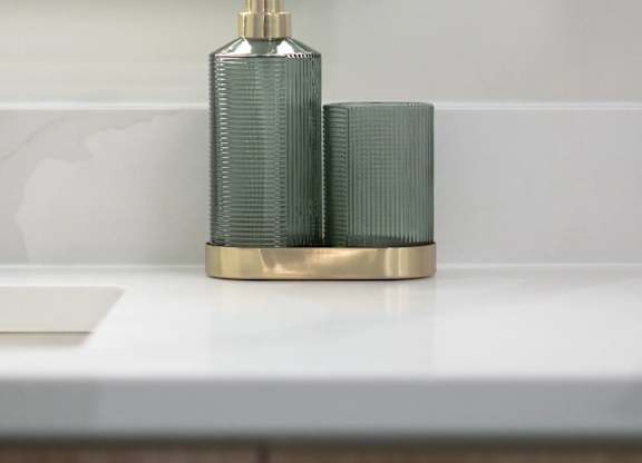A gold soap dispenser with a green pump sits on a white countertop.