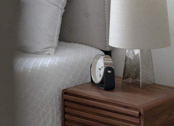A clock sits on a nightstand next to a bed.