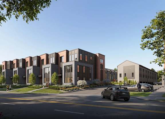 A modern building with a red brick facade is surrounded by greenery and parked cars.