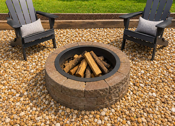 Two chairs are placed around a fire pit on a gravel patio.