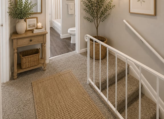A hallway with a staircase, a mirror, a potted plant, and a basket on the floor.