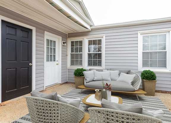A grey house with a white door and a grey couch on the patio.