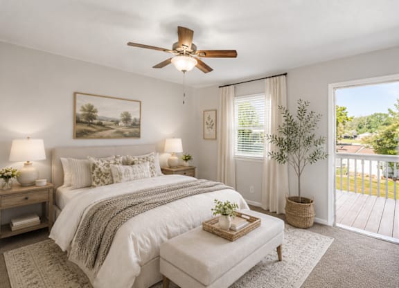 A bedroom with a large bed, a ceiling fan, and a view of the backyard through the window.