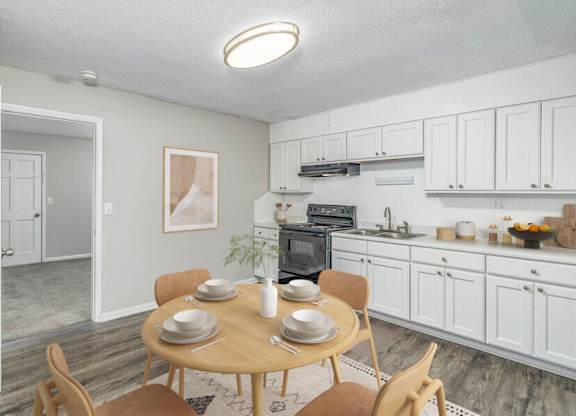 A dining room with a table set for two and a kitchen in the background.