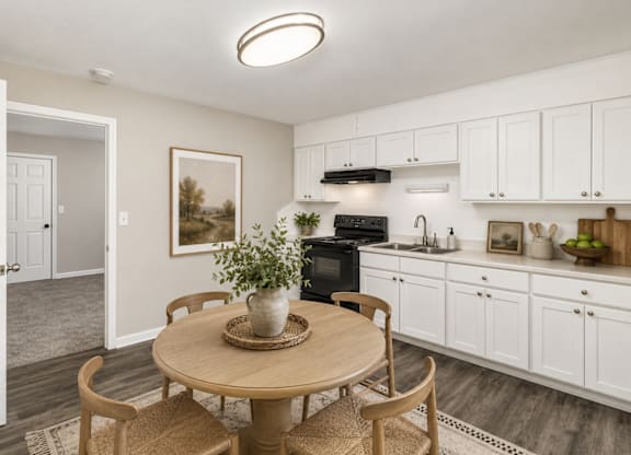 A kitchen with a table and chairs in the foreground and a framed picture on the wall.