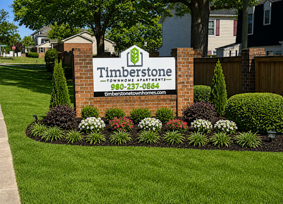 A sign for Timberstone Townhome Apartments is surrounded by flowers and greenery.