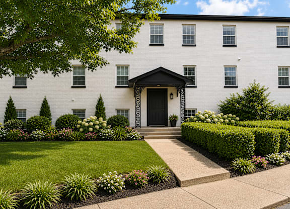 A white building with a black door and windows surrounded by greenery.