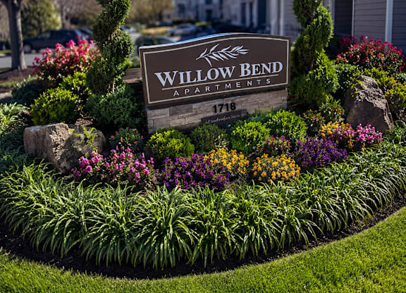 A sign that says Willow Bend in front of a flower bed.