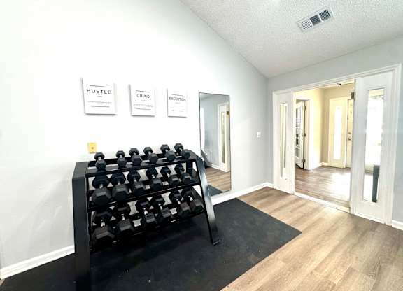 A black dumbbell rack is in the corner of a room with a mirror and three signs on the wall.