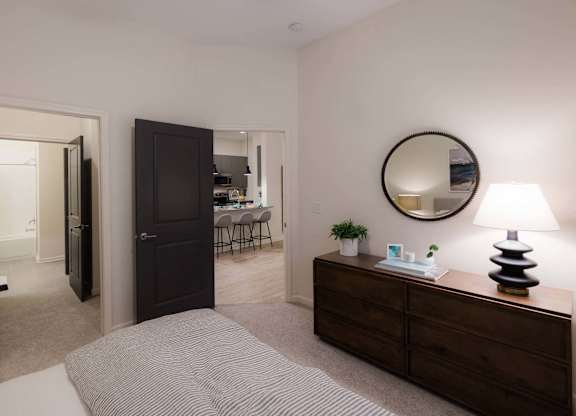 A bedroom with a bed, dresser, mirror, and lamp at Hudson at Renaissance Apartments, North Carolina 28405