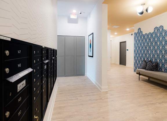 A hallway with a row of black lockers on the left and a bench with a blue and white patterned wall behind it on the right at Hudson at Renaissance Apartments, Wilmington