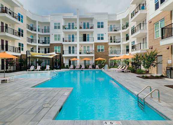 A large swimming pool in a residential building surrounded by lounge chairs and umbrellas at Hudson at Renaissance Apartments, North Carolina